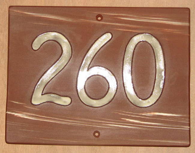 plaque rectangulaire couleur chocolat décorée par deux bandes de fils de porcelaine blanche en haut et en bas portant au centre, en gros, émaillé en blanc, le numéro de la maison.